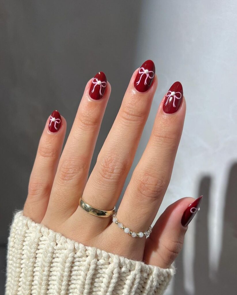 Deep glossy red nails along with a delicate white bow painted near the center of each nail