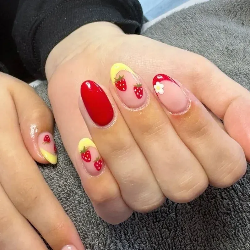 oval nails with a yellow French tip and a tiny red strawberry.