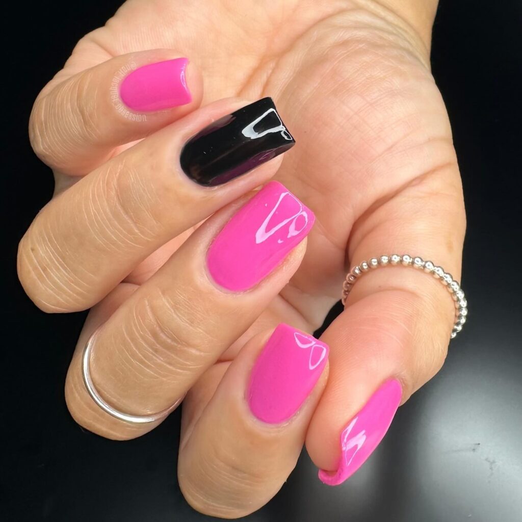 A hand with bright neon pink nails accept the ring finger; which is painted in black