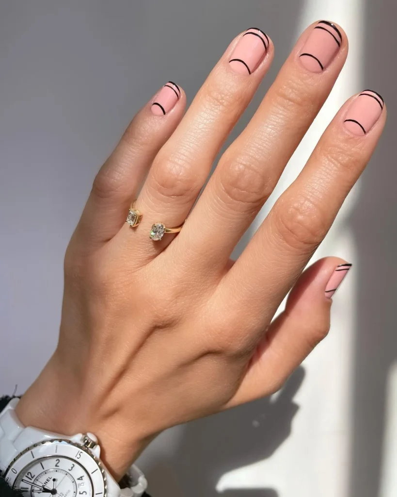 Short nail painted in nude color with three thin curved  line in black color.