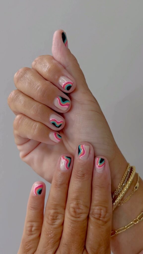 Colorful nail art with squiggly lines in pink, blue, and black on a neutral base of short natural nails