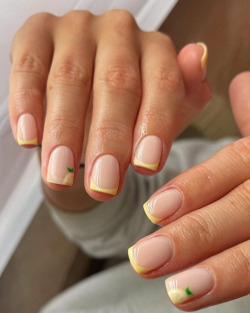 Little nails with a yellow French tip and a small lemon design on the accent nail.