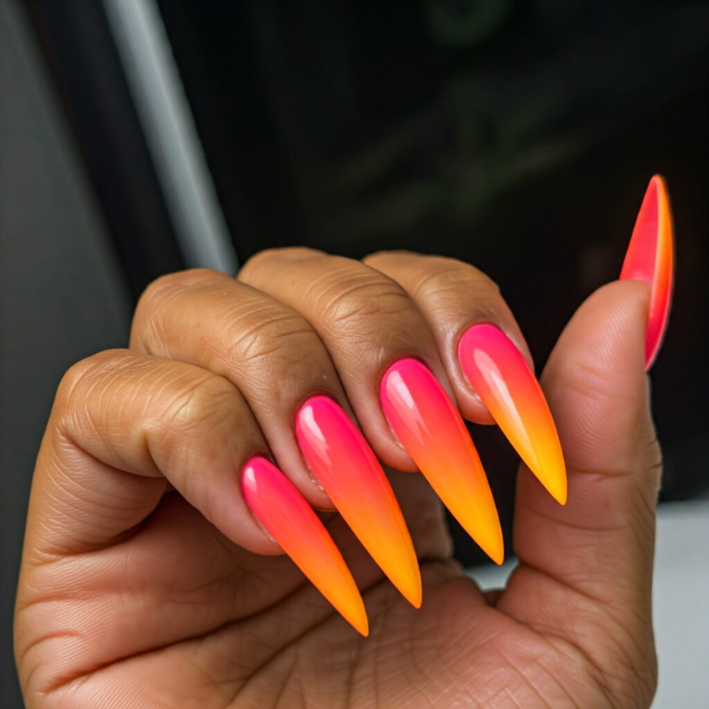 a medium tone hand with long, stiletto-shaped nails painted in a gradient of pink, orange, and yellow.