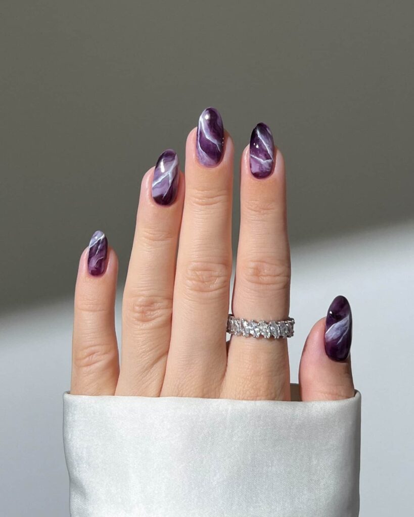 Almond-shaped nails with a purple and white marble design resembling amethyst